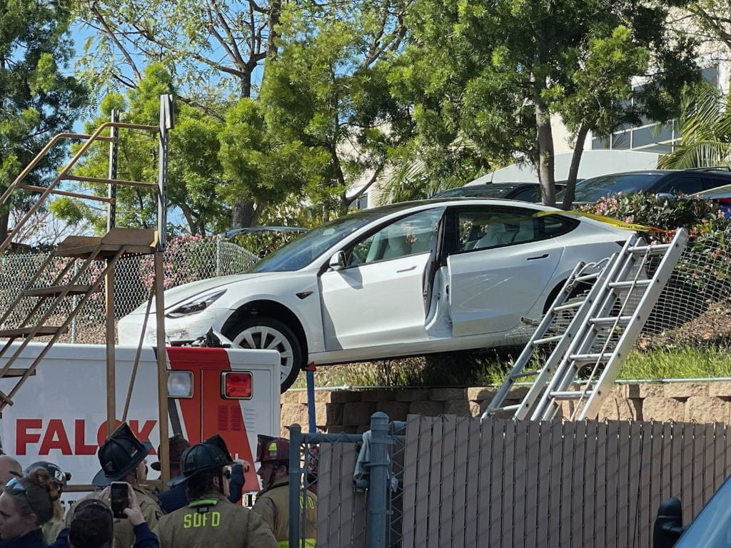 A driver and two passengers were injured Wednesday when the Tesla they were riding in crashed down a small embankment and landed on top of an ambulance in parking lot in Kearny Mesa.